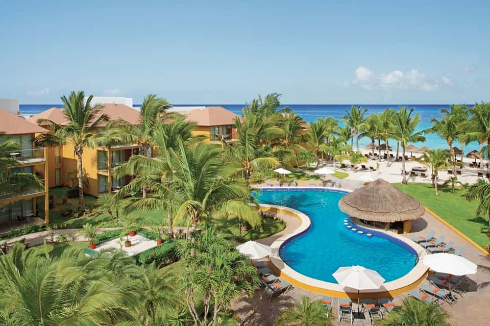 Aerial view of beachfront resort with curved swimming pools, palm trees, and sandy beach