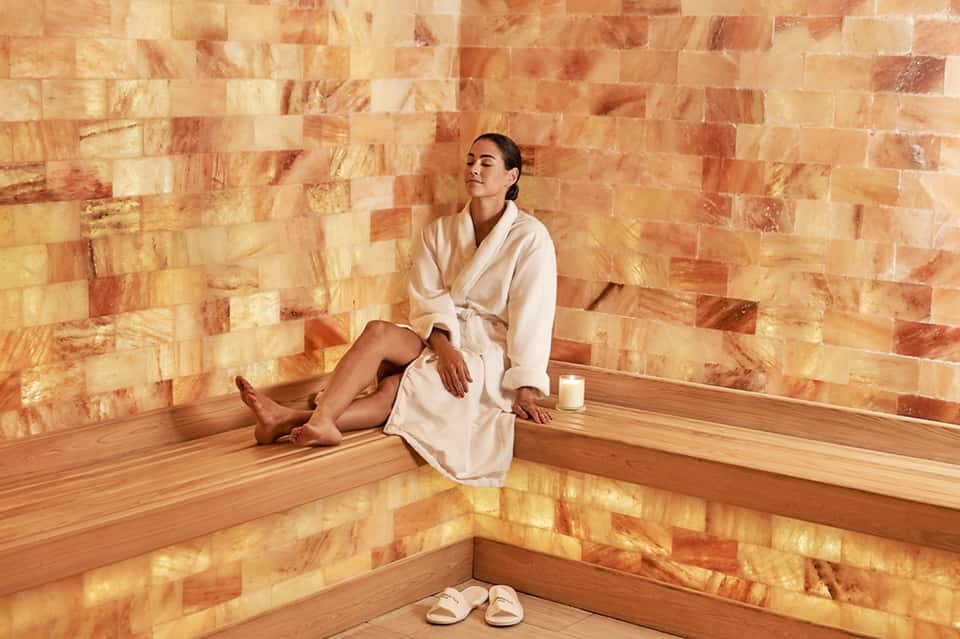 Woman in cream robe relaxing in wooden sauna with salt brick wall
