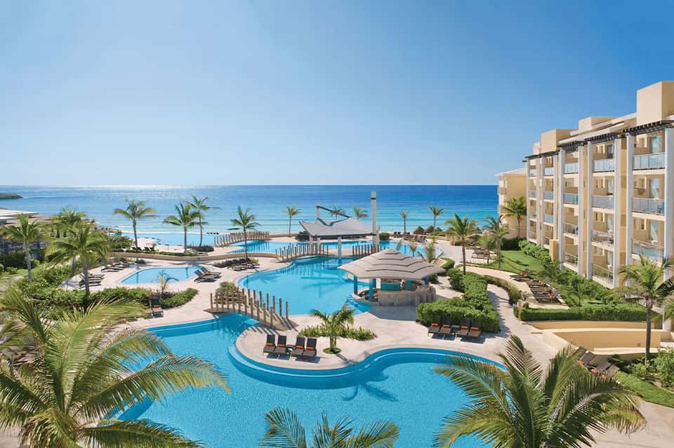 Expansive resort pool complex with curved sections, loungers, beachfront, and ocean views with palm trees