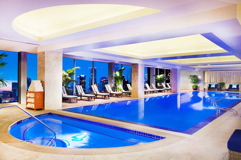Indoor pool and spa with blue water, lounge chairs, and city skyline views