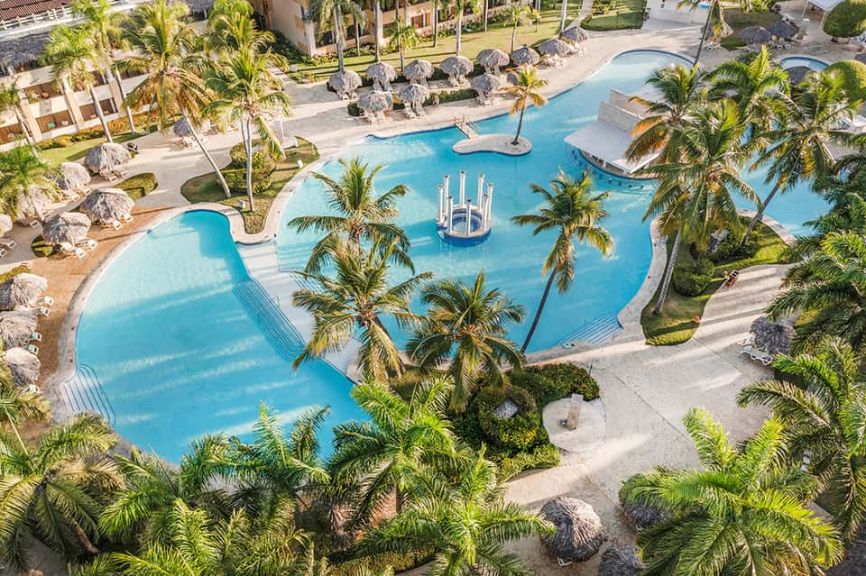 Aerial view of large resort pool complex with blue water, palms, and beach loungers
