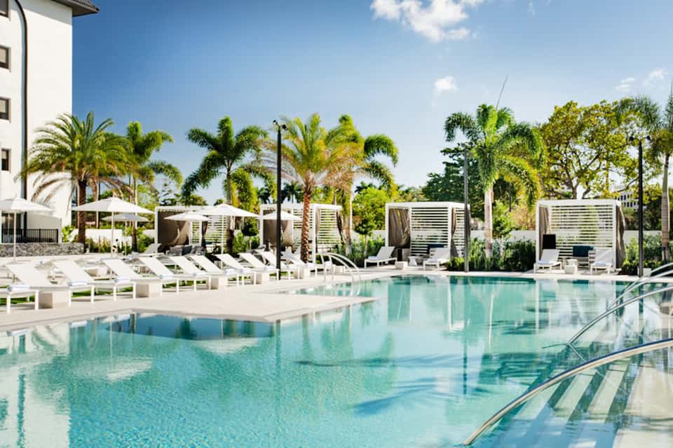 Resort pool with palm trees, white lounge chairs, and cabanas in daytime