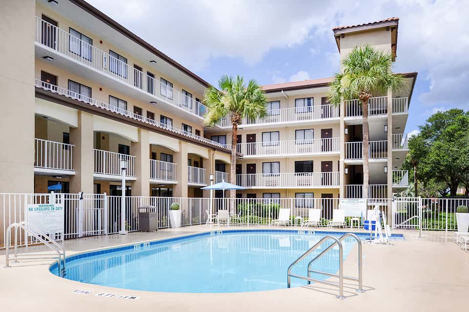 Resort courtyard with kidney-shaped pool, multi-story building, and palm trees