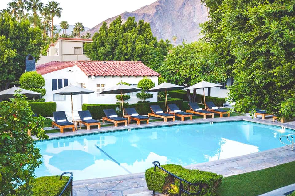 Resort pool with lounge chairs, umbrellas, white cabana, and mountain backdrop