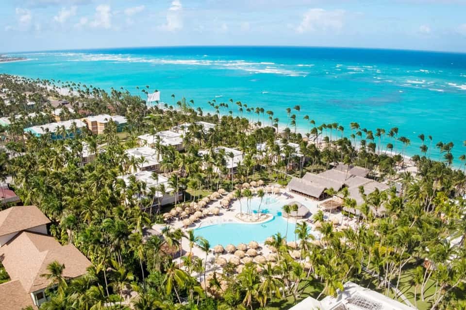 Aerial resort view showing buildings, pools, palm trees and pristine turquoise Caribbean beach