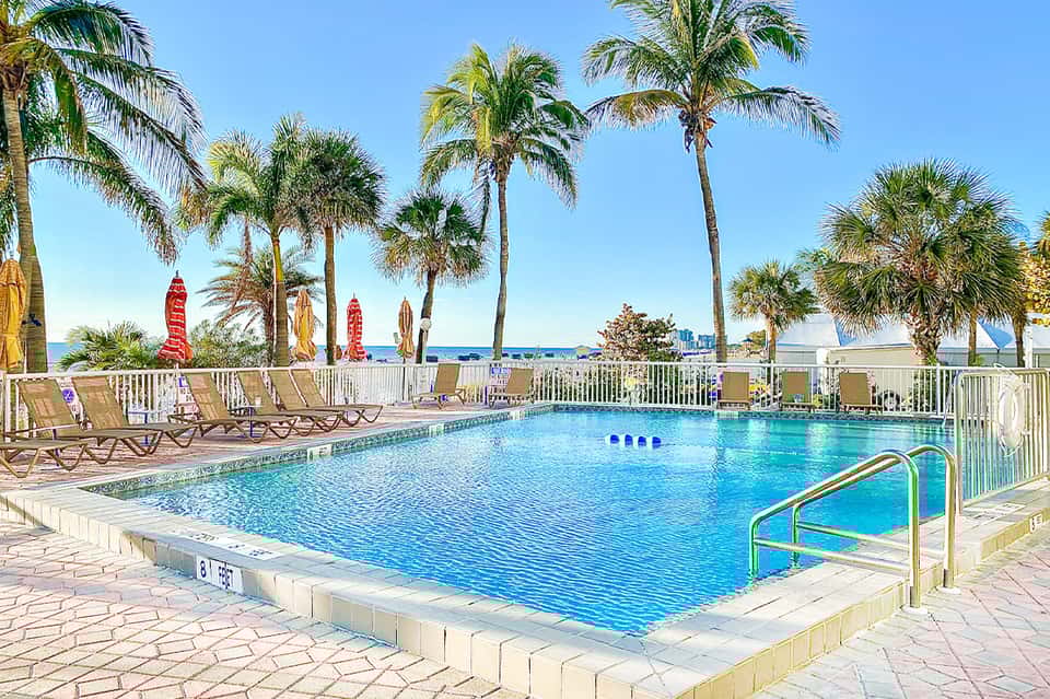 Beachfront swimming pool with loungers, palm trees, surfboard decorations, ocean view