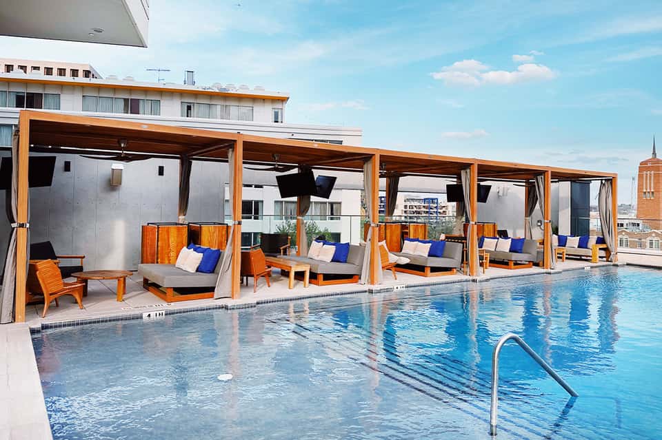 Modern rooftop pool with orange cabanas, blue cushioned seating, and city skyline in background