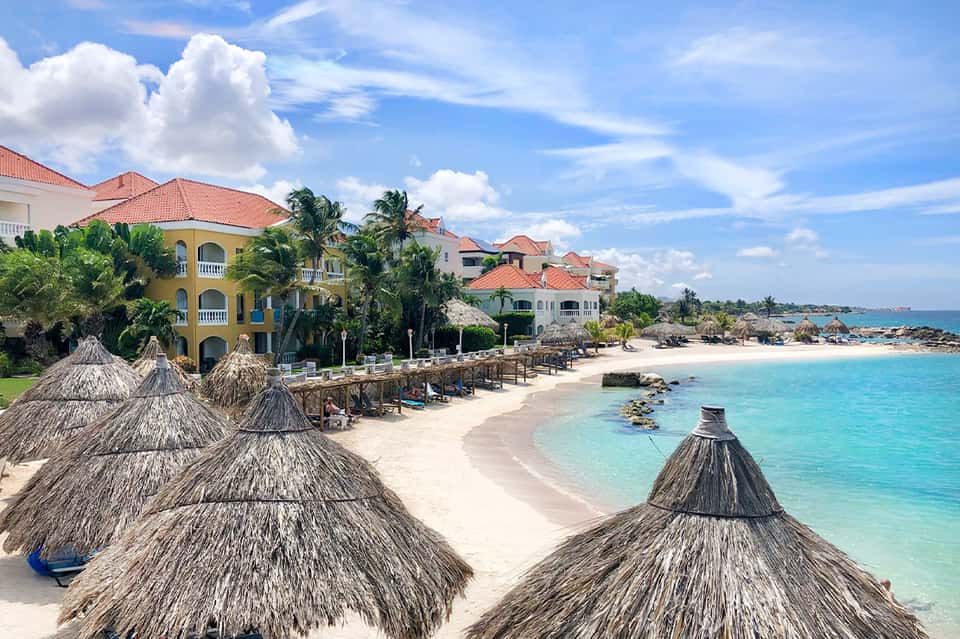 Beachfront resort with colorful colonial buildings, thatched umbrellas, and crystal-clear turquoise water