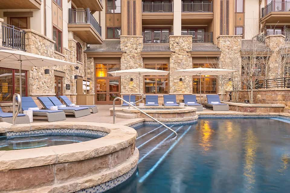 Resort pool courtyard with stone facade, loungers with blue cushions, and hot tub