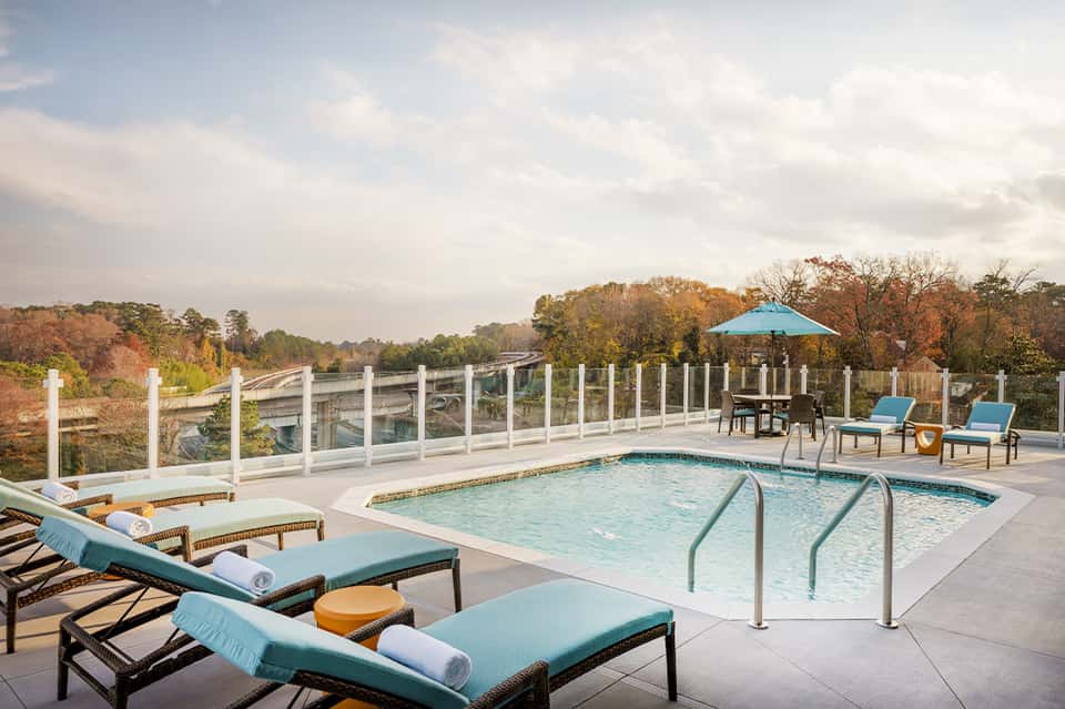 Residential pool on elevated deck with glass railings, lounge chairs, umbrella, and forest views