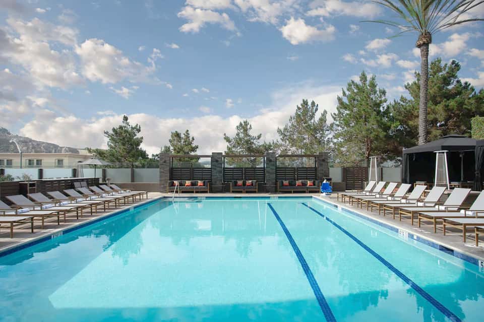 Lap pool with lane markers, lounge chairs, black privacy screens, and mountain backdrop