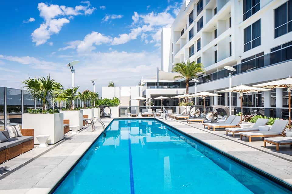 Contemporary pool with lap lanes, lounge chairs, white umbrellas, and hotel building