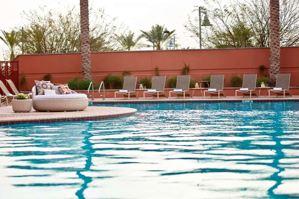 Resort pool with terracotta accent wall, lounge chairs, and palm trees in background