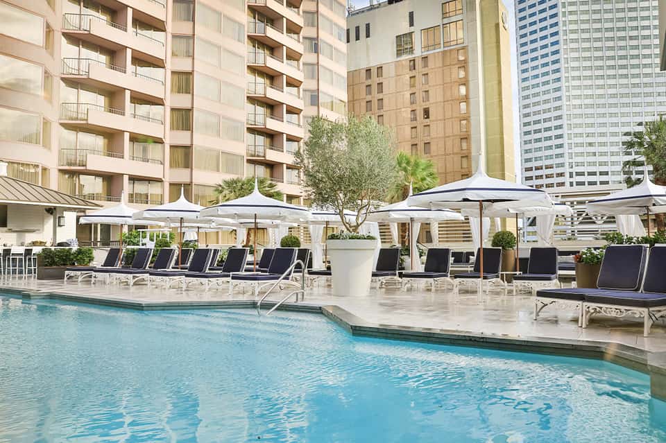 Urban resort pool with white umbrellas, lounge chairs, and surrounding tall buildings