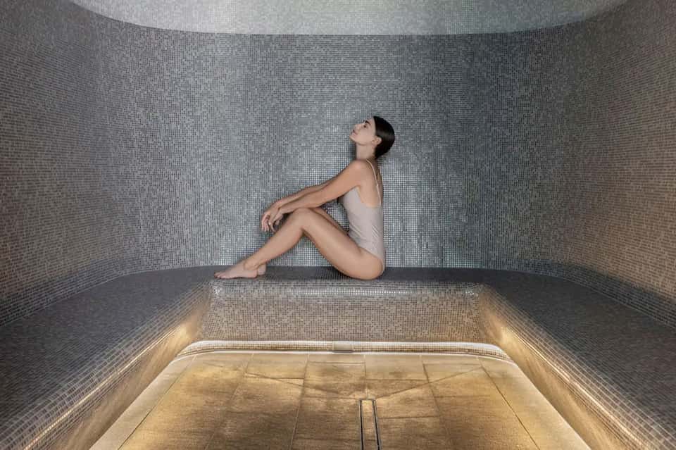 Woman sitting in tiled steam room or spa facility with minimalist interior design
