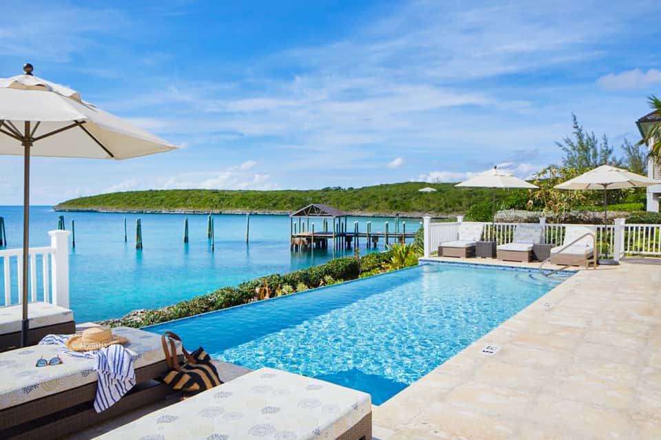 Oceanfront infinity pool with white umbrellas, private dock, and lush green cove beyond