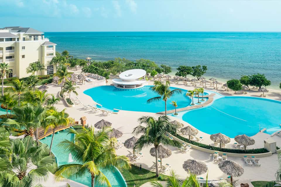 Beachfront resort with curved swimming pools, palm trees, and crystal-blue Caribbean waters