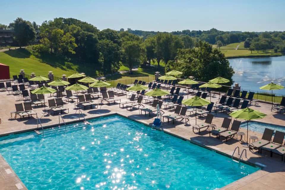 Resort pool surrounded by loungers, green umbrellas, and scenic waterfront landscape