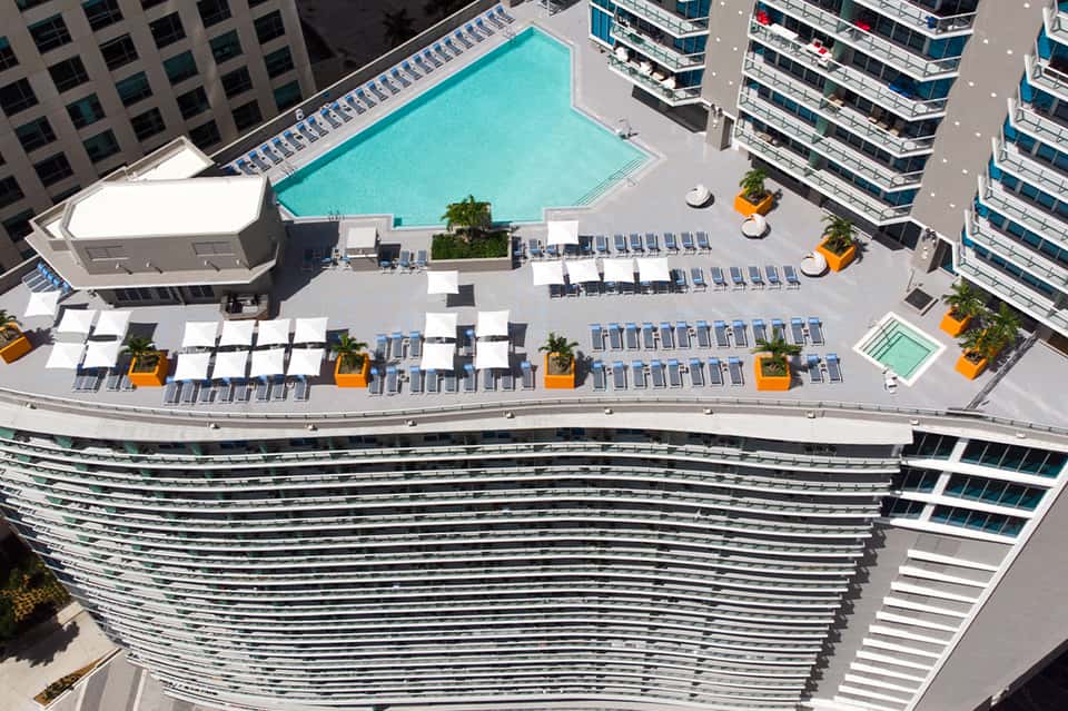 Aerial view of urban resort pool deck with turquoise pool, lounge chairs, and surrounding high-rise buildings