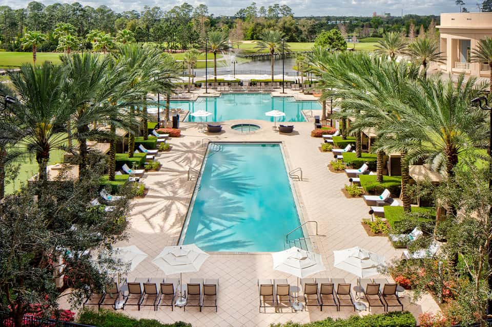 Resort pool complex with palm trees, loungers, fire pit, and manicured grounds