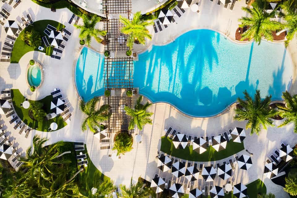 Overhead view of resort pool with curved turquoise water, surrounding lounge chairs, palms, and geometric patio layout