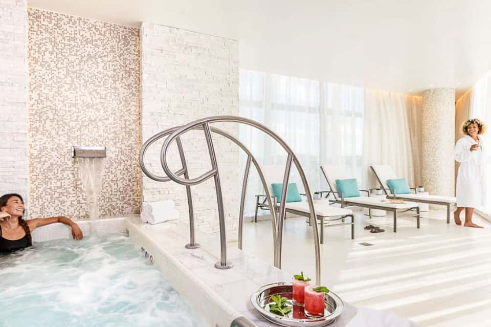 Luxury spa with hot tub, arched metal railings, mosaic tile walls, and lounge chairs in bright white space