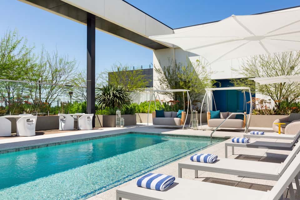Contemporary pool with white shade sails, loungers, modern furniture, and palm trees