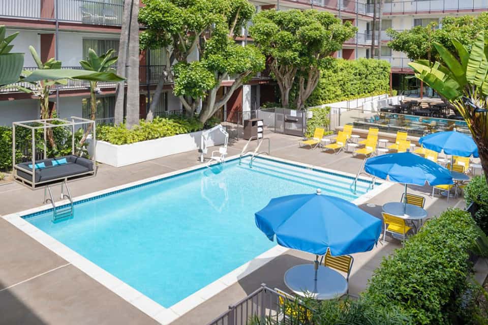 Urban resort courtyard pool with blue umbrellas, yellow lounge chairs, and surrounding buildings