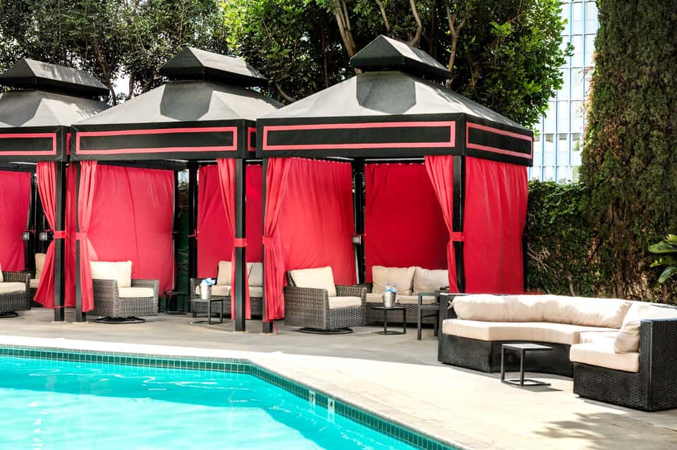 Poolside red and black cabanas with white cushioned seating and concrete deck