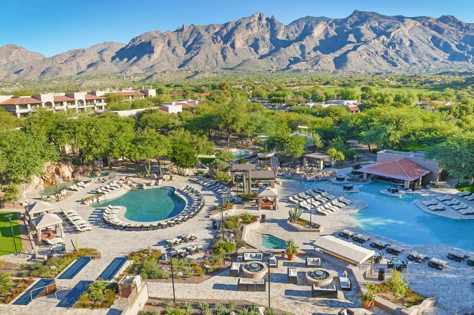Aerial view of desert resort with multiple pools, loungers, and mountain landscape backdrop