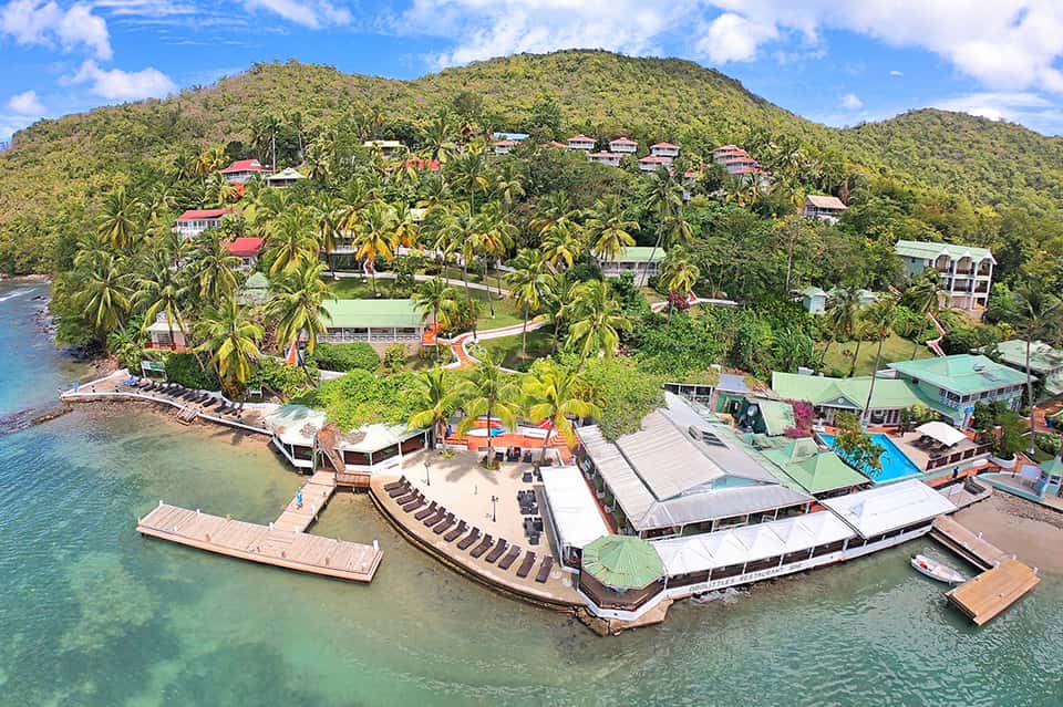 Aerial view of tropical beachfront resort with colorful buildings nestled in lush green hillside