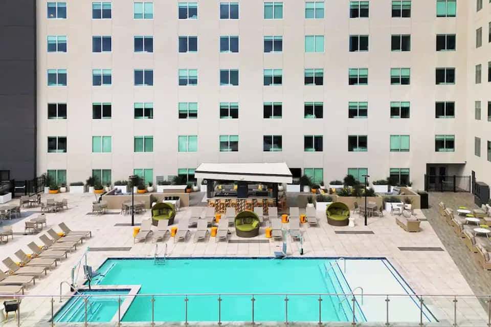 Urban hotel courtyard pool with modern architecture, lounge chairs, and green planters