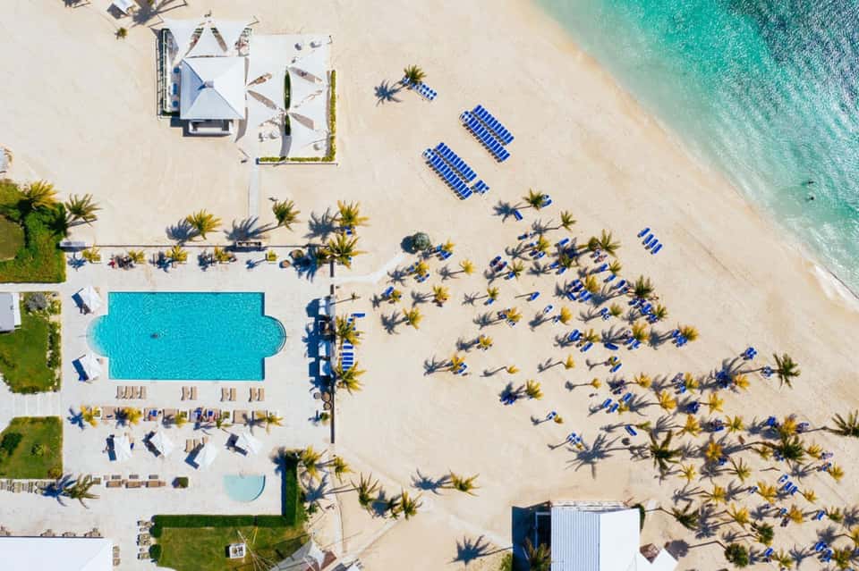 Beachfront resort aerial view with pool, umbrellas, palm trees, and clear ocean