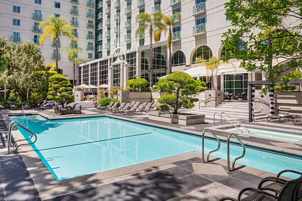 Resort courtyard pool surrounded by hotel building, lounge chairs, and topiary