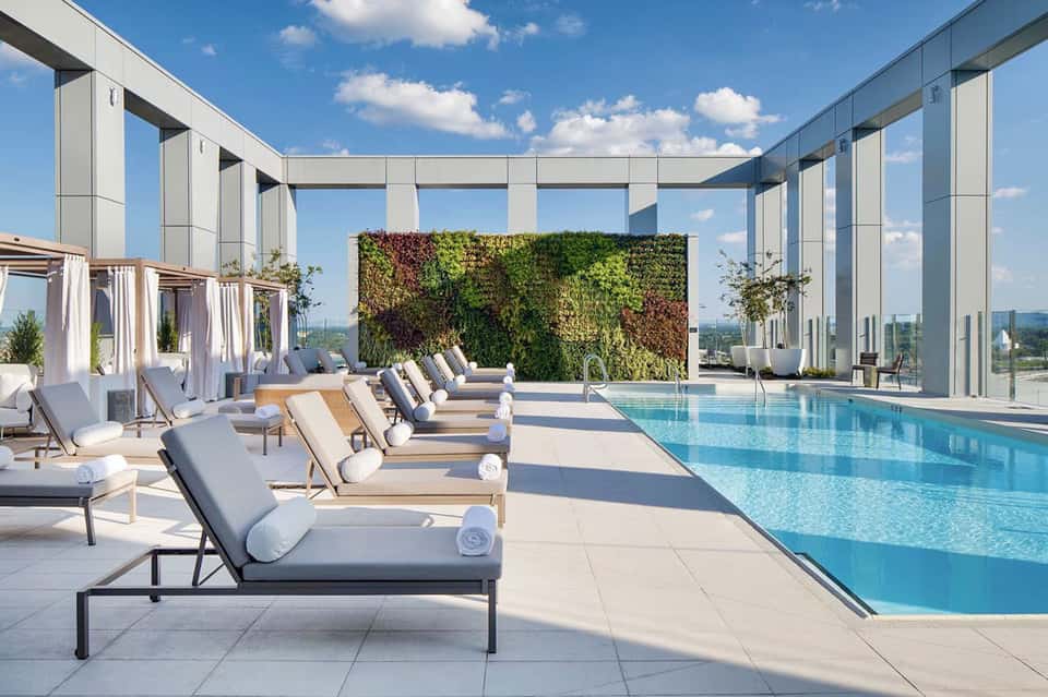 Modern rooftop infinity pool with lounge chairs, living plant wall, and panoramic city views