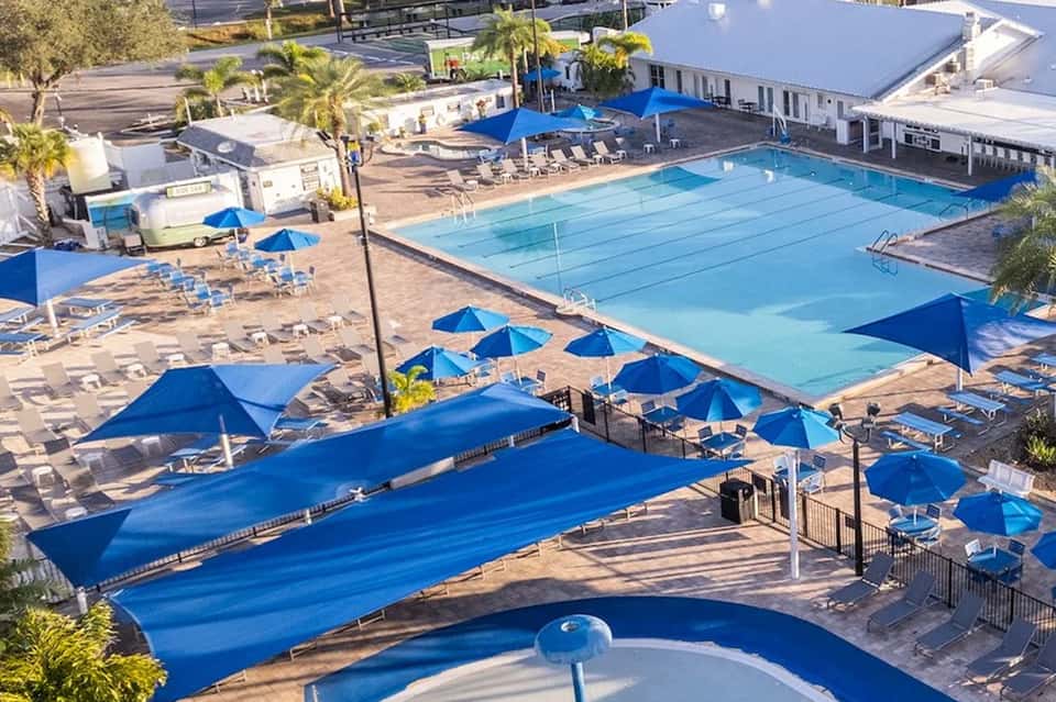 Aerial view of resort pools with blue umbrellas, lounge chairs, palm trees, and facilities