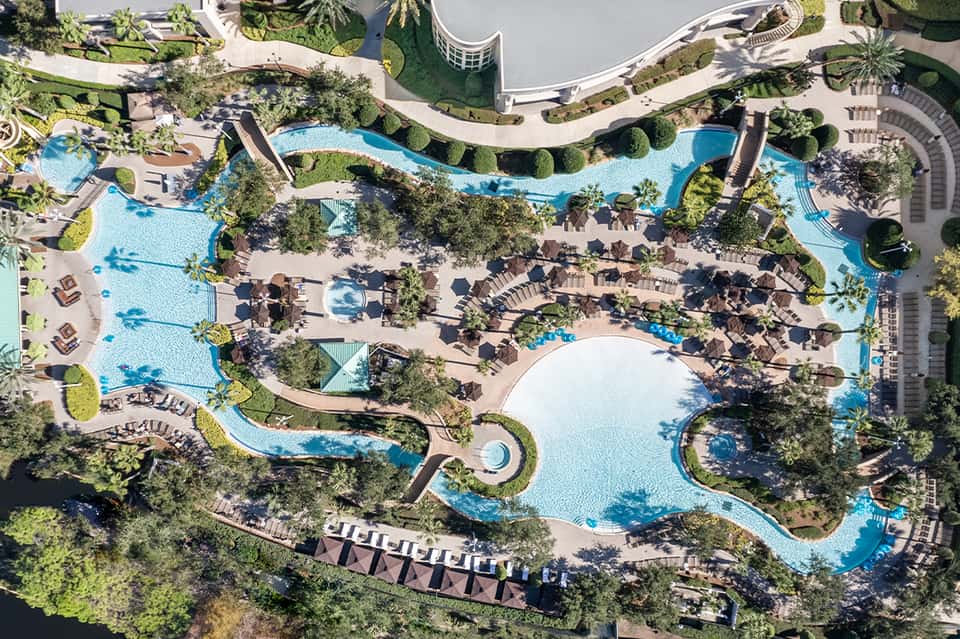 Overhead view of sprawling resort with multiple blue pools, loungers, and palm tree landscaping