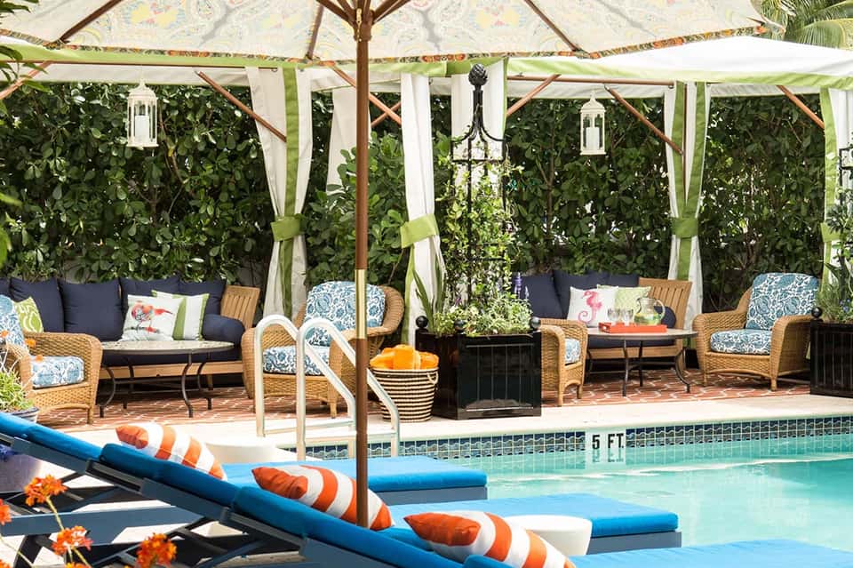 Upscale poolside lounge with wicker seating, pergola shade, and manicured tropical gardens