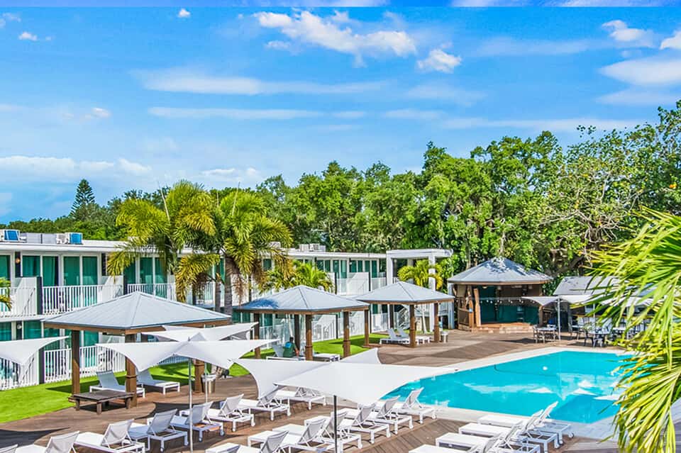 Resort pool with loungers, white umbrellas, and modern cabanas surrounded by greenery