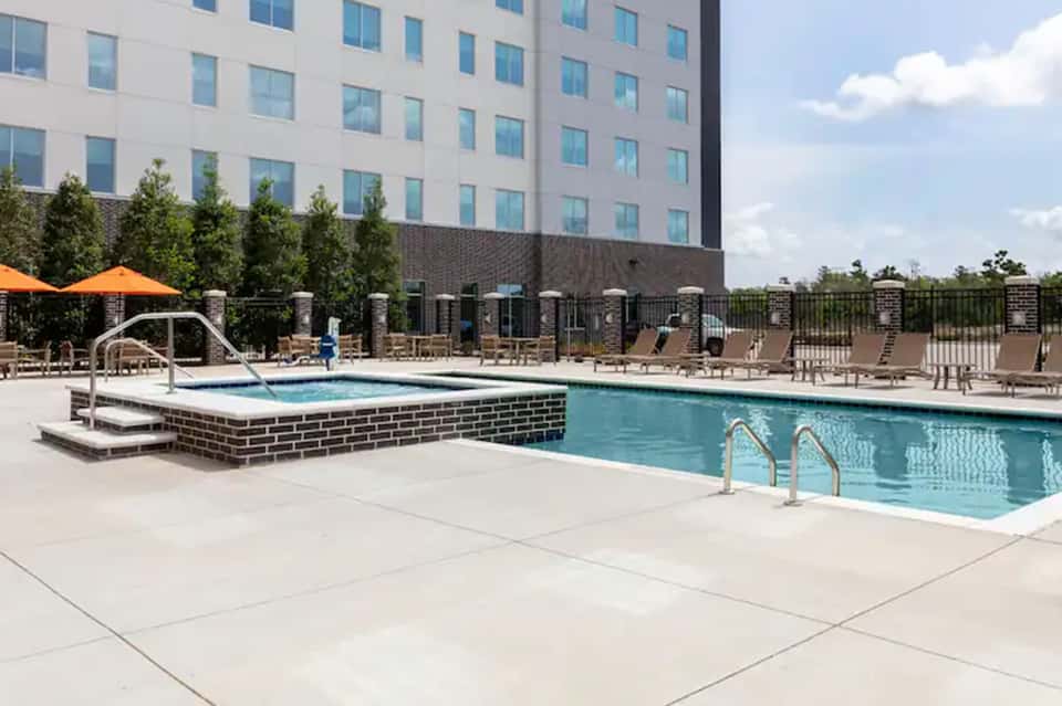 Contemporary hotel pool with spa jet feature, loungers, orange umbrellas, brick building, and manicured landscaping