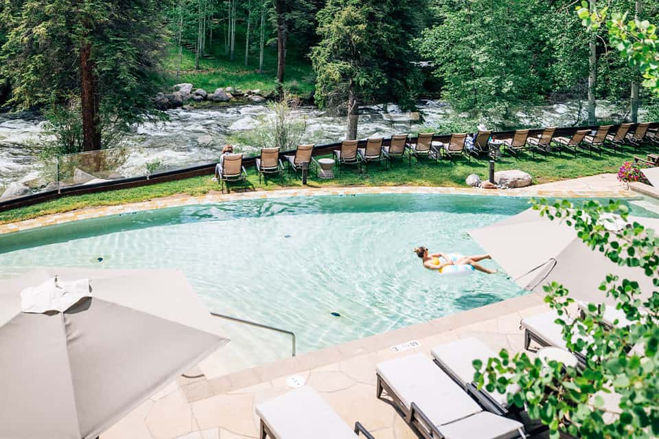Resort pool in forest setting with lounge chairs and mountain river backdrop