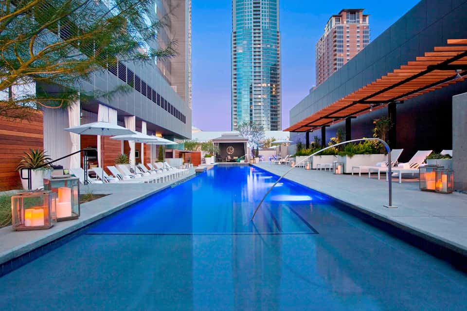 Modern urban resort pool at dusk with blue water, lounge chairs, and downtown buildings