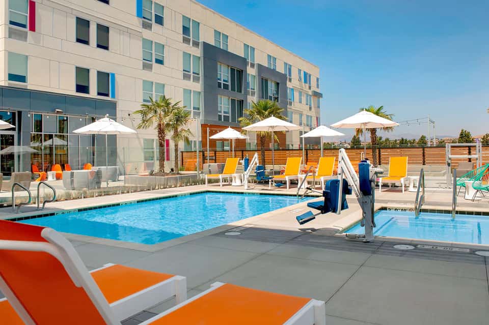 Contemporary hotel pool with orange loungers, white umbrellas, and colorful modern building