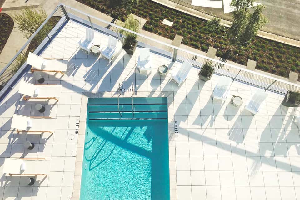 Aerial view of rectangular swimming pool surrounded by white lounge chairs and glass barriers on sunny terrace