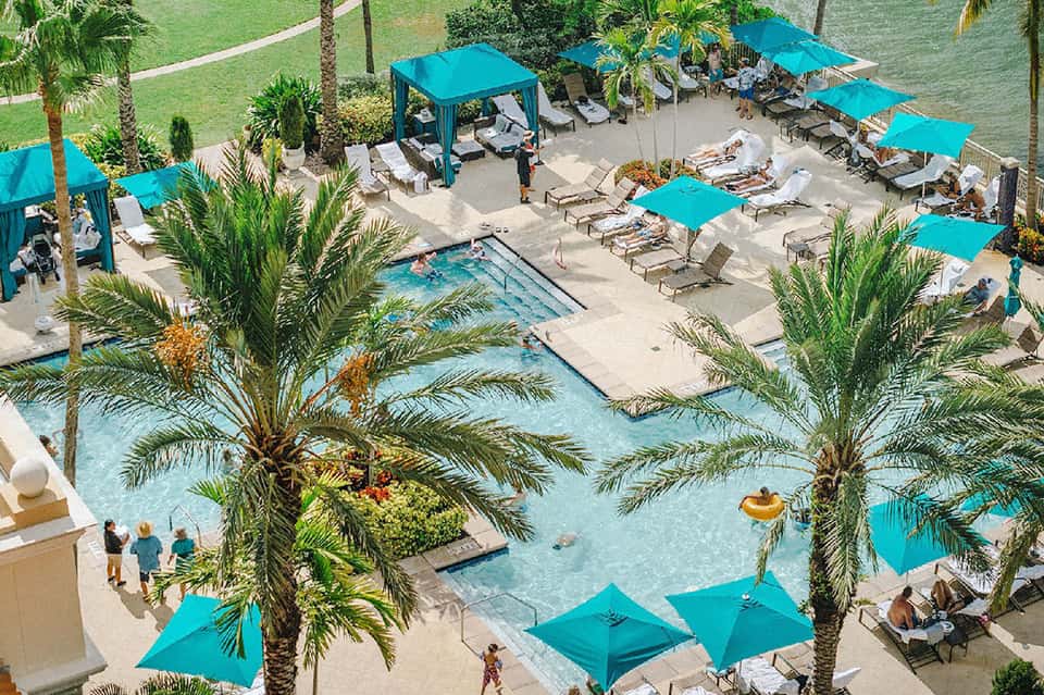Aerial view of resort pool deck with bright turquoise umbrellas, loungers, and palm trees