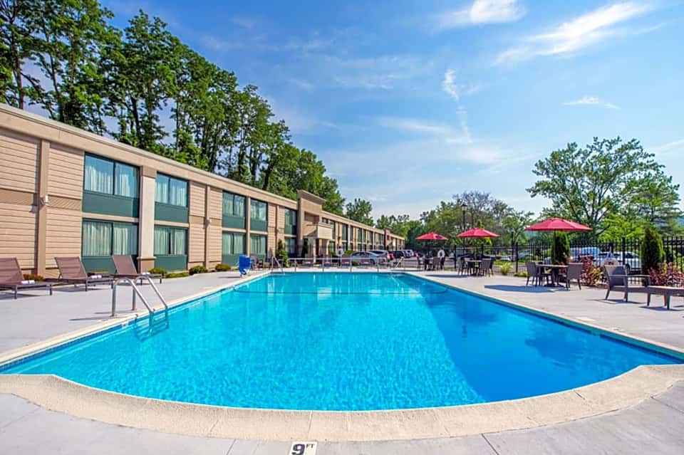 Resort swimming pool with curved edges, blue water, and adjacent motel-style accommodations with red umbrellas