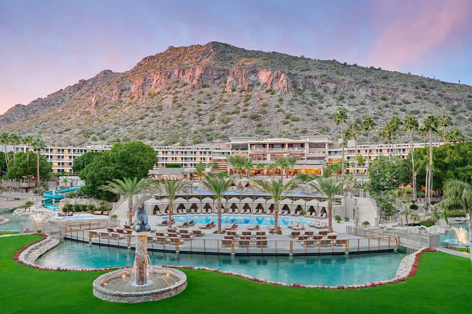 Sprawling desert resort with multiple pools, palm trees, mountain backdrop, and modern architecture