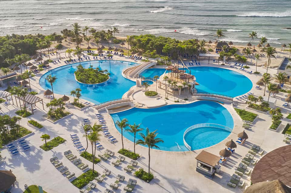 Large resort complex with multiple curved pools, loungers, beach access, and tropical landscaping