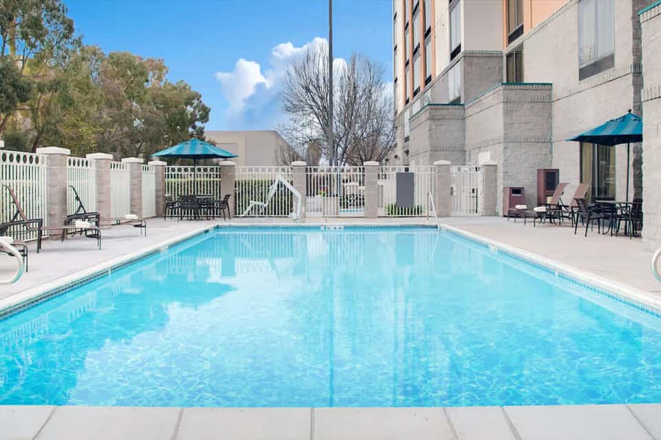 Clean rectangular outdoor swimming pool with white loungers and white fence enclosure