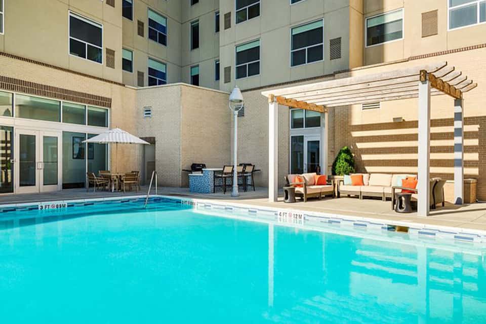 Indoor courtyard pool with lounge seating, white pergola shade structure, and surrounding hotel building